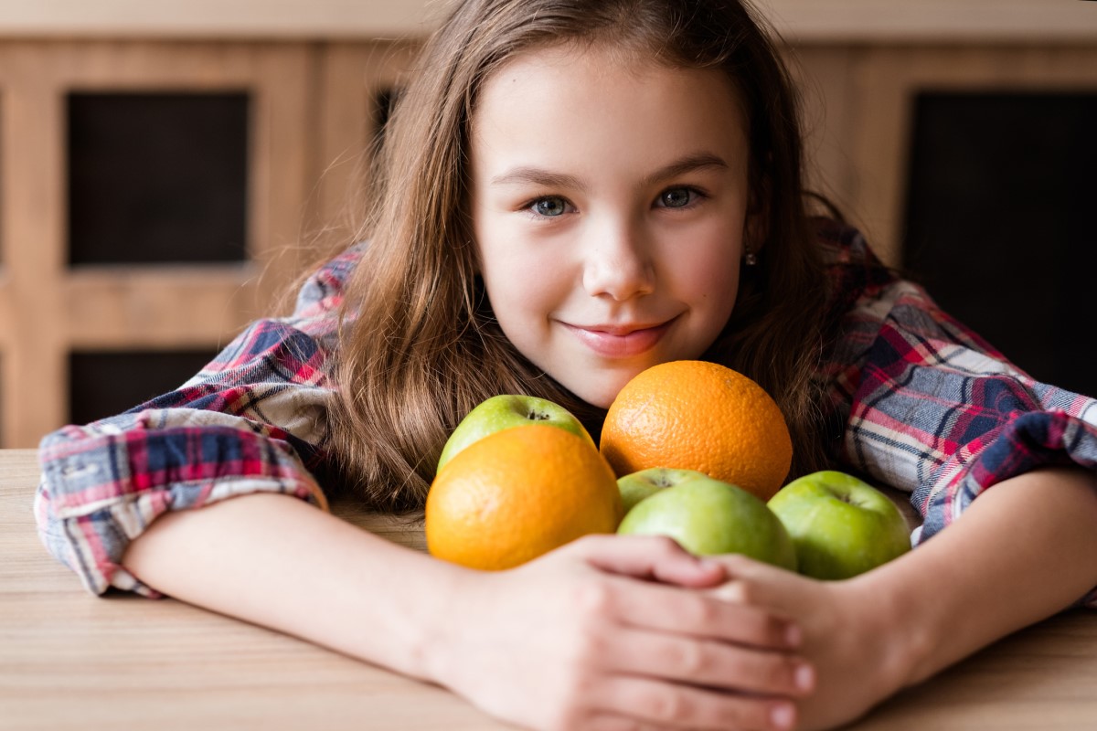 C-vitamin, gyümölcsökben, egy gyermek, aki narancsot és almát tart a karjában.