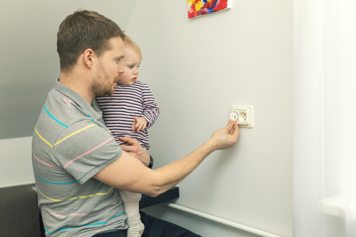 Apa karjában tartja a kisgyereket, és elektromos dugóval zárja le a dugót.