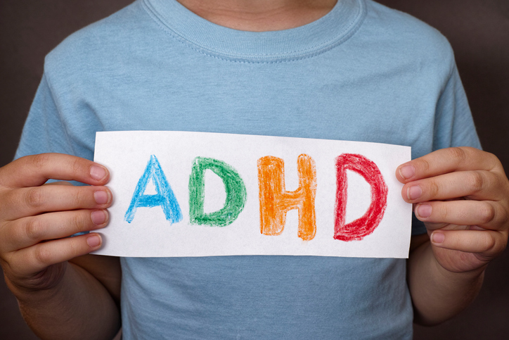 Egy fiú egy színes ADHD feliratú táblát tart a kezében.