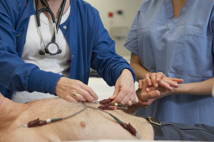 A férfi EKG-vizsgálata, elektródák a mellkasán, két orvos vizsgálja őt.